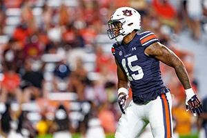 A football player in an Auburn uniform jogs on the field during a game, with a blurred crowd in the background.