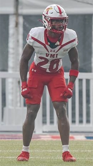 A football player in a red and white VMI uniform stands in a defensive stance, ready for action on the field.